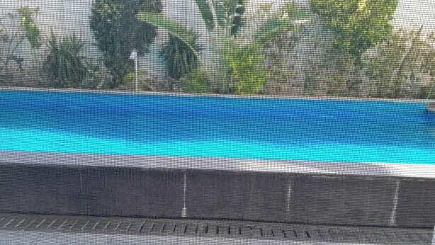A swimming pool with a clear blue water surface, surrounded by a tiled deck and a mesh fence. - Spacious and Modern one bed in Hurhgarda (Hurghada)