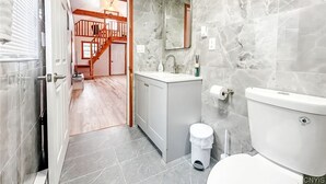 A modern bathroom with grey marble walls, a wooden staircase leading to a loft, and a white toilet. - Charming cottage Pulaski VIP Rentals 1.8 miles away from famous salmon river (Pulaski)