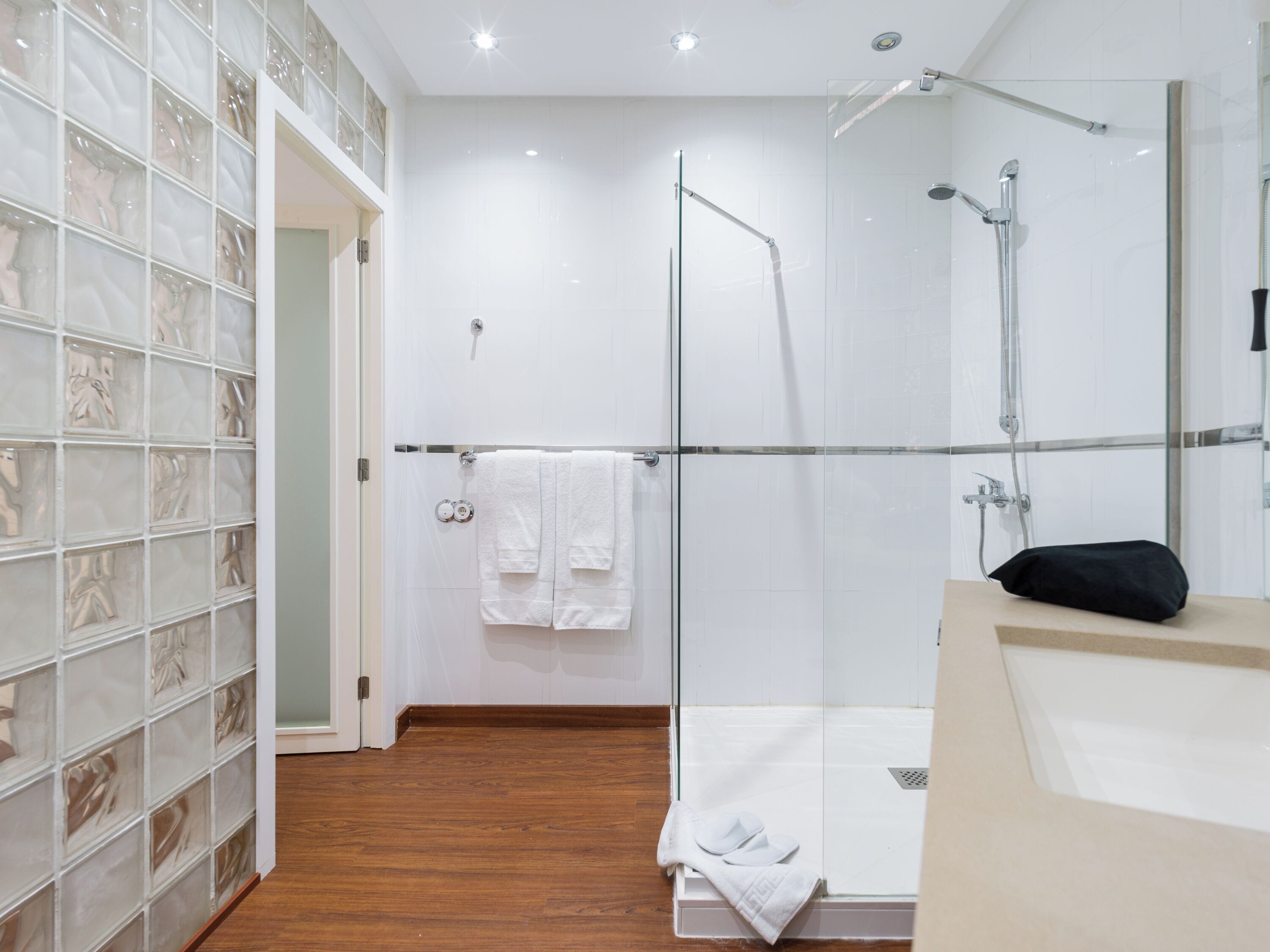A modern bathroom with a glass shower enclosure, a wooden floor, and a white sink with a black towel.
