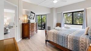 Ein Schlafzimmer mit einem großen Bett, einem Schminktisch, einem Deckenventilator und Blick ins Freie durch eine Schiebetür.
