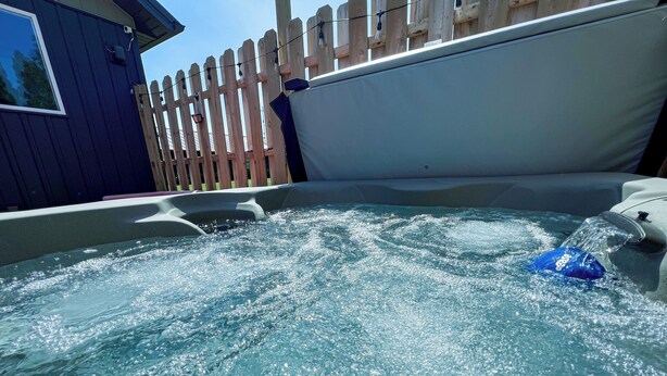 Ein Whirlpool mit spritzendem Wasser, umgeben von einem Holzzaun und einem Gebäude.