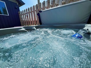 Una bañera de hidromasaje con agua salpicando, rodeada de una valla de madera y un edificio.