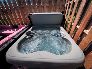 A hot tub with a control panel, surrounded by a wooden fence and pink outdoor seating. - Hot Tub Cabin Hideaway Near Tomahawk (Irma)