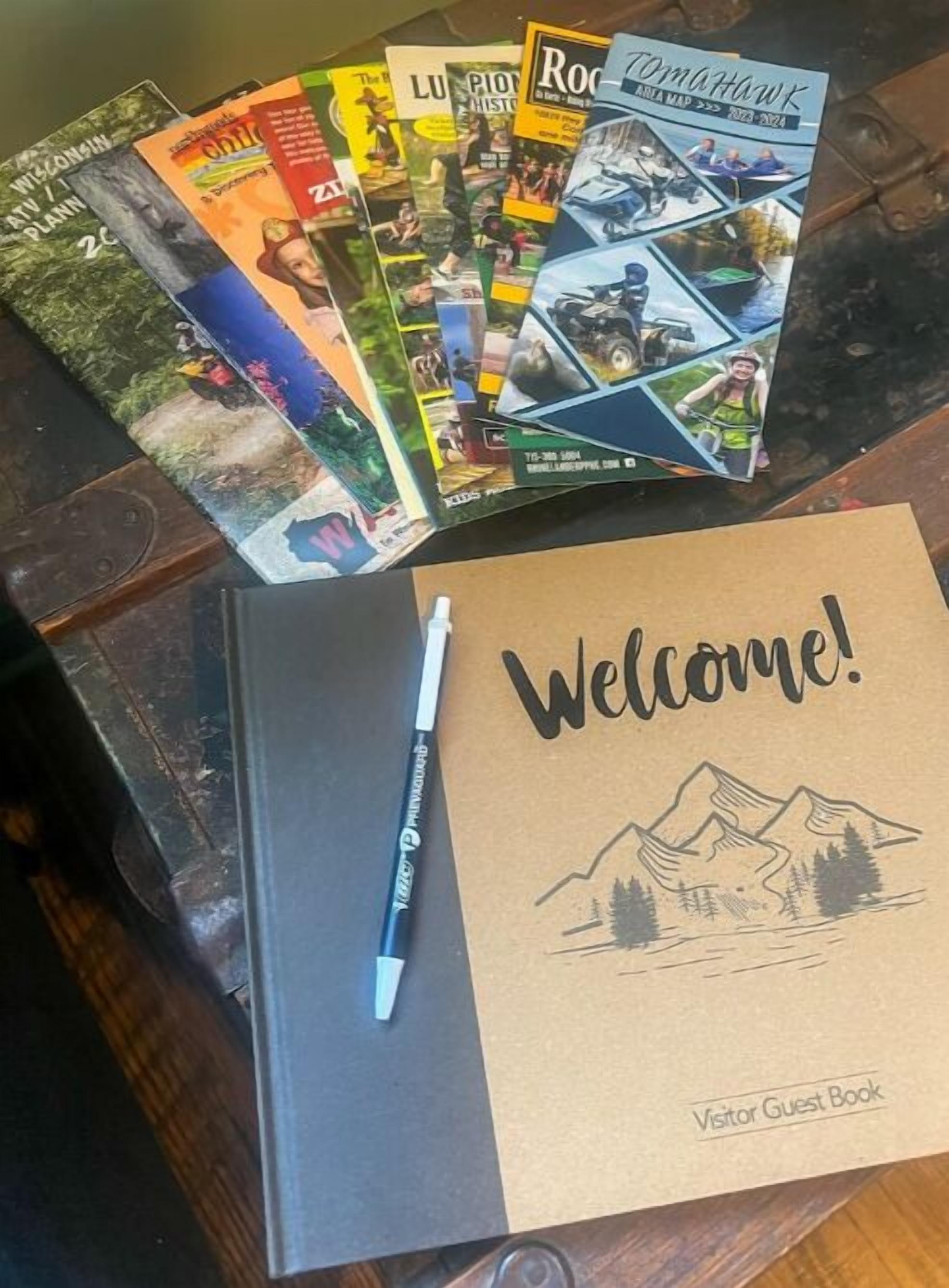 A stack of travel brochures and a visitor guest book on a wooden table.