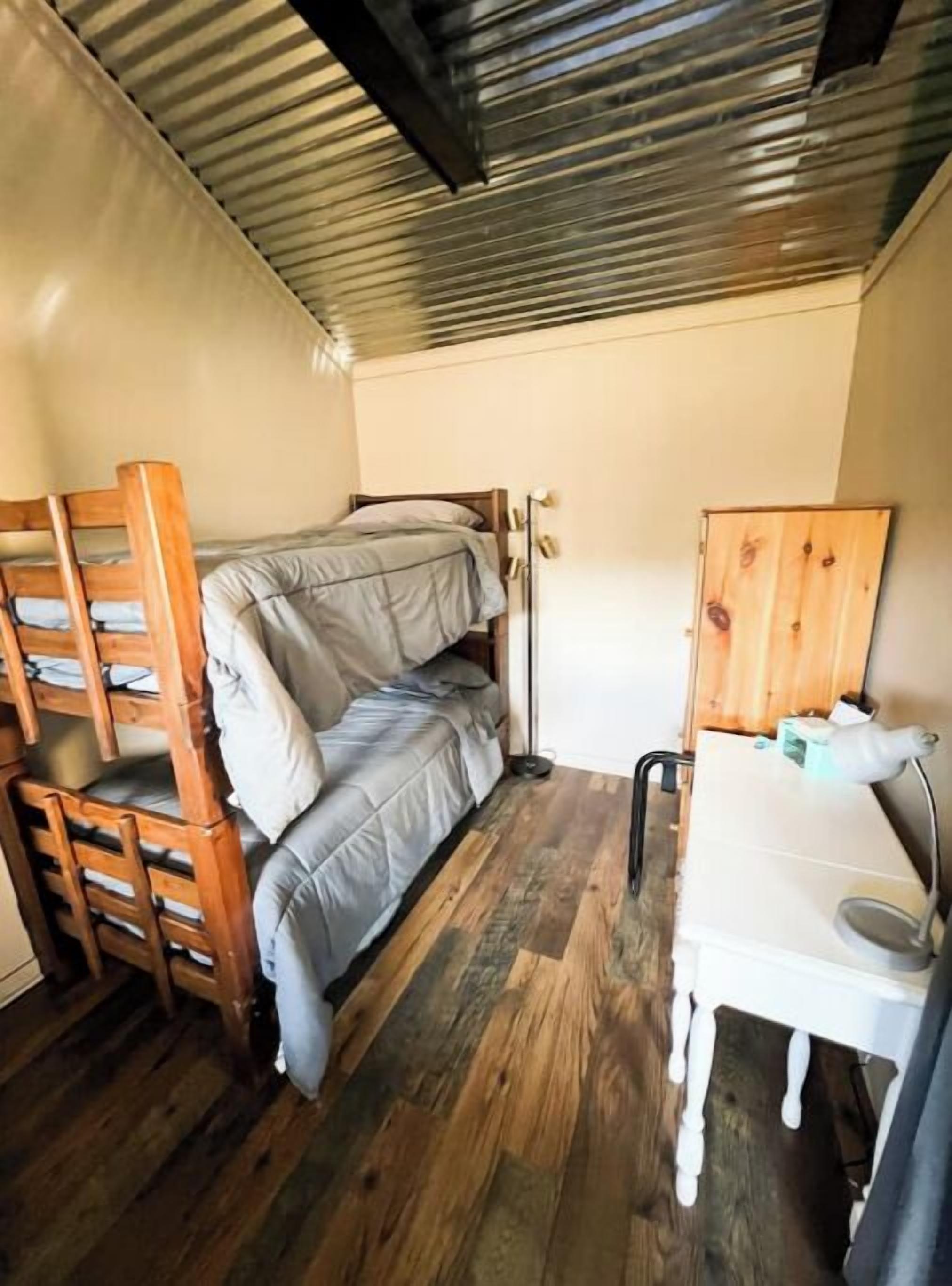 Habitación compacta con una cama litera, un escritorio con silla y un lavamanos pequeño y blanco.