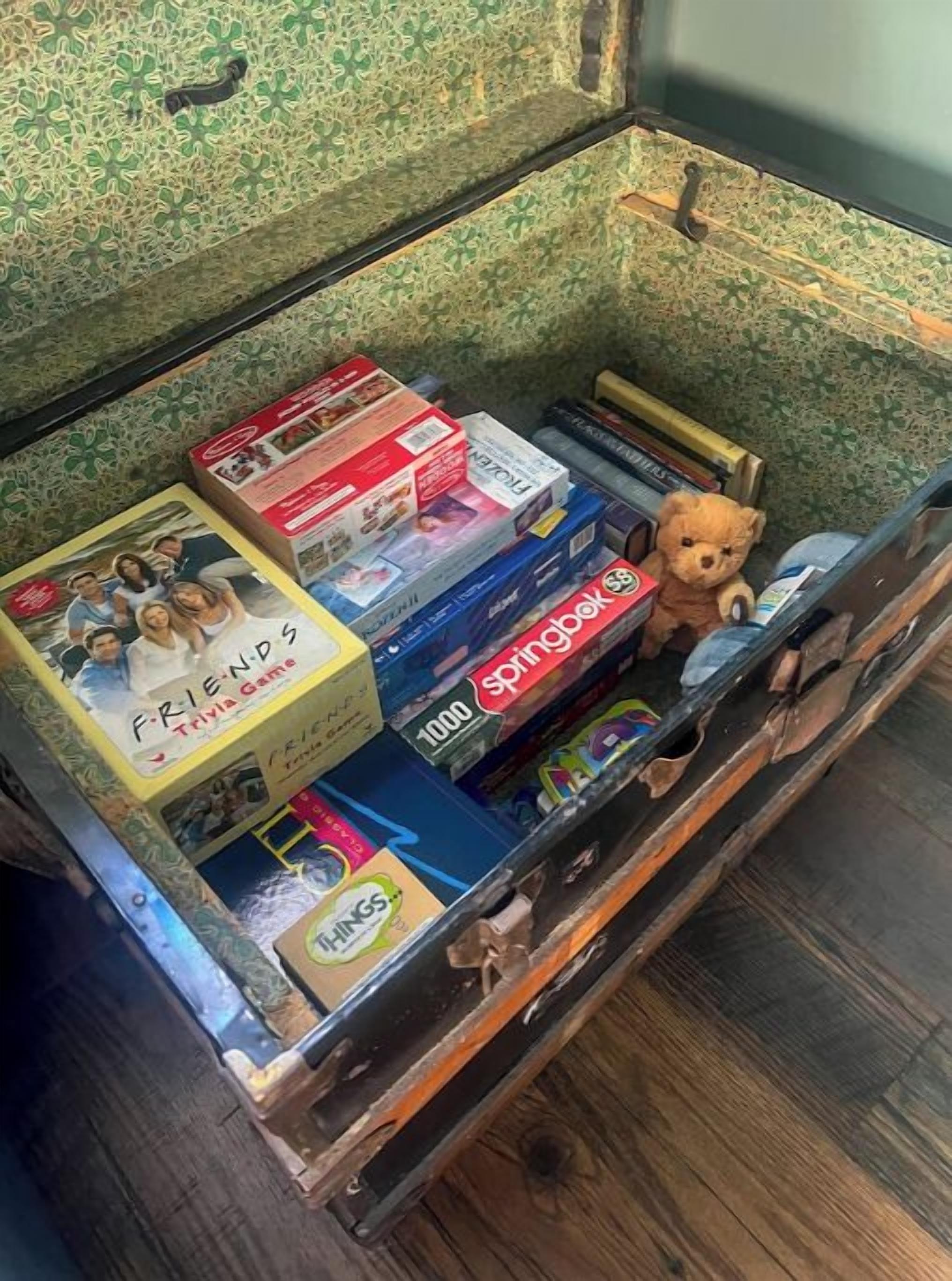 Un baúl antiguo lleno de varios juegos de mesa y un oso de peluche.