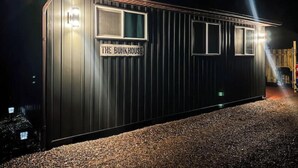 Ein Gebäude aus Metall mit dem Schild "THE BUNKHOUSE", nachts beleuchtet durch Scheinwerfer.
