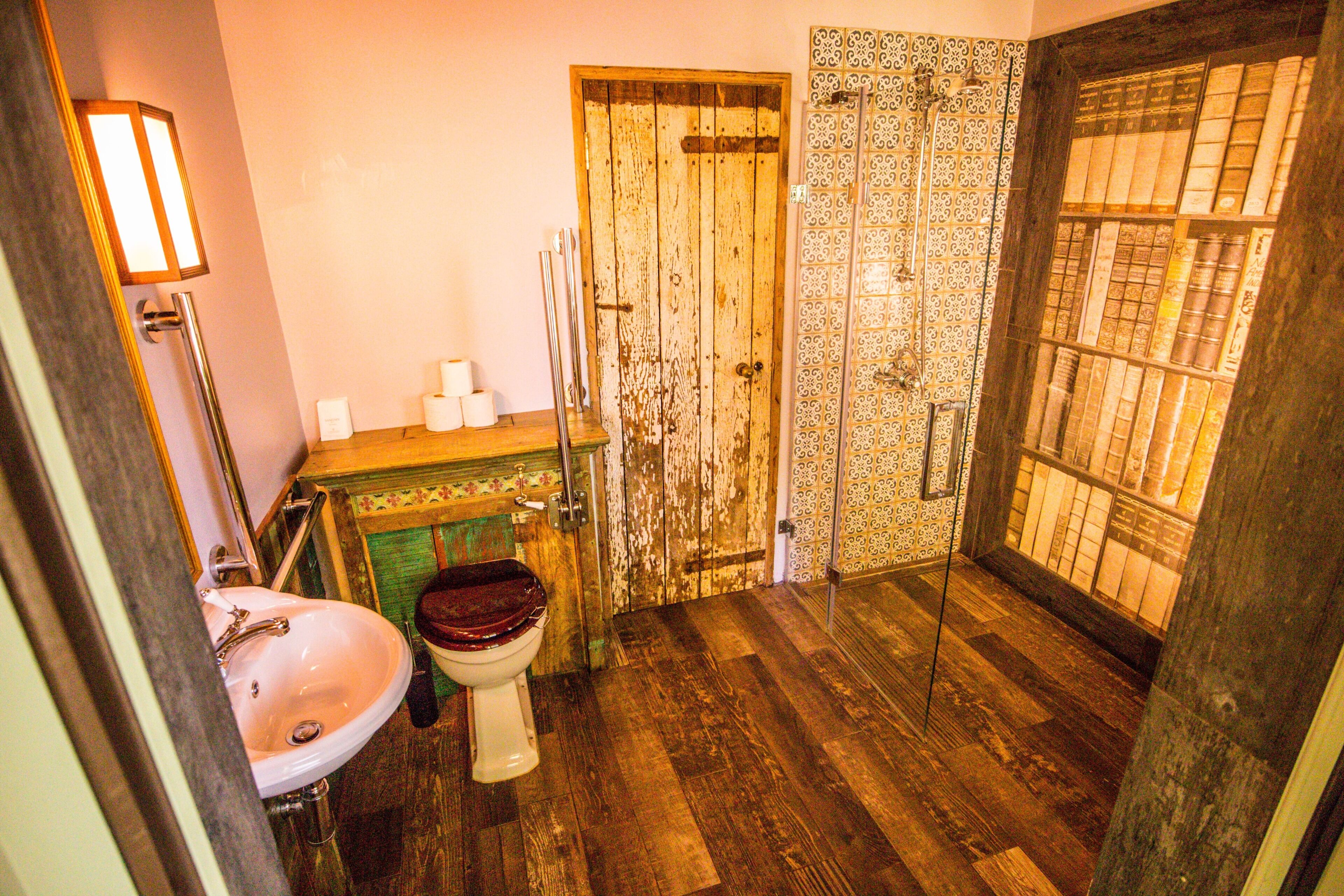 Un baño con suelo de madera, un lavamanos blanco y una puerta de madera con un ventanal de vidrio decorado.