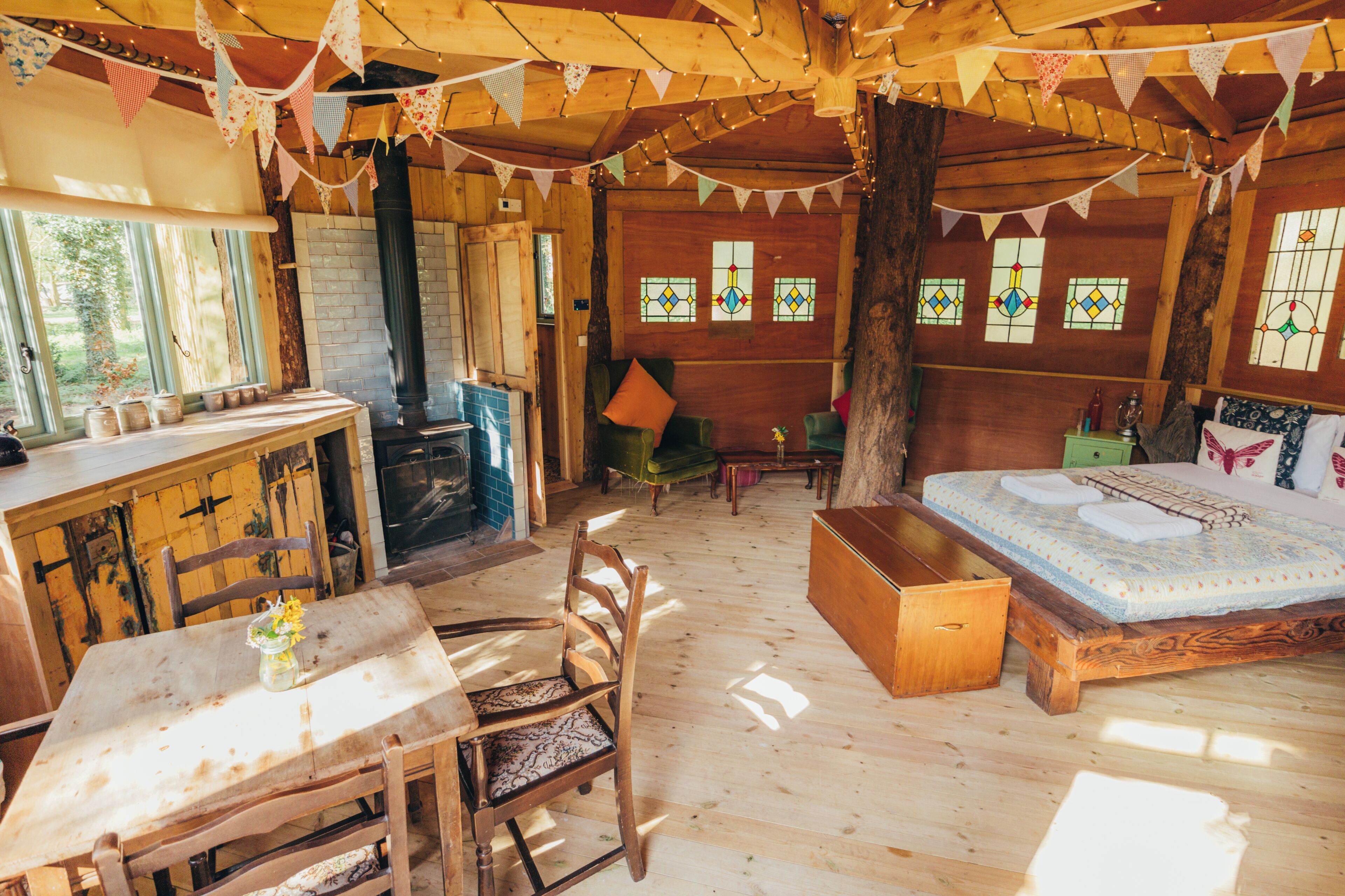 Une pièce rustique en bois, avec un lit, une table, des chaises, une cheminée et des vitraux.