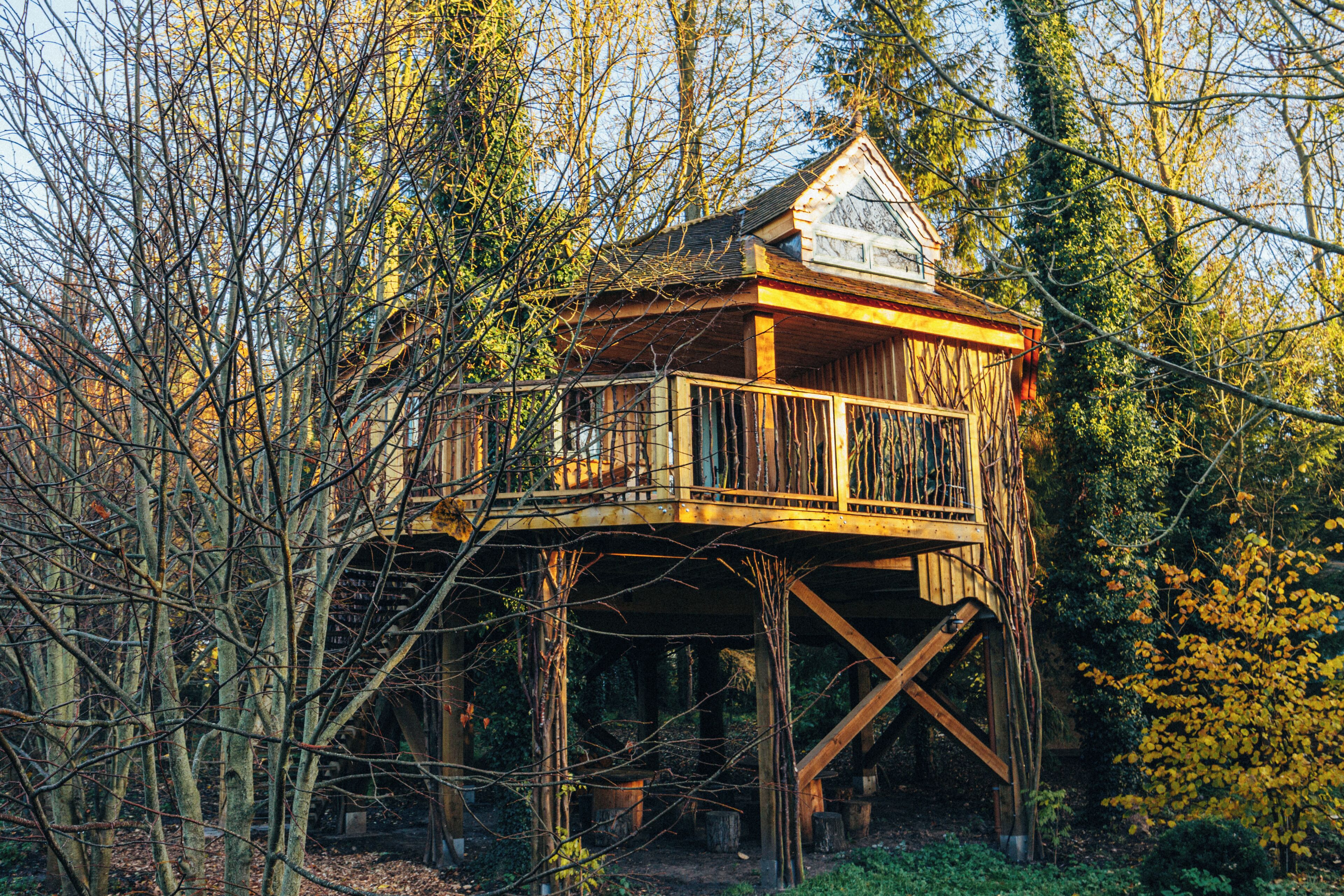A wooden treehouse with a balcony, surrounded by trees.