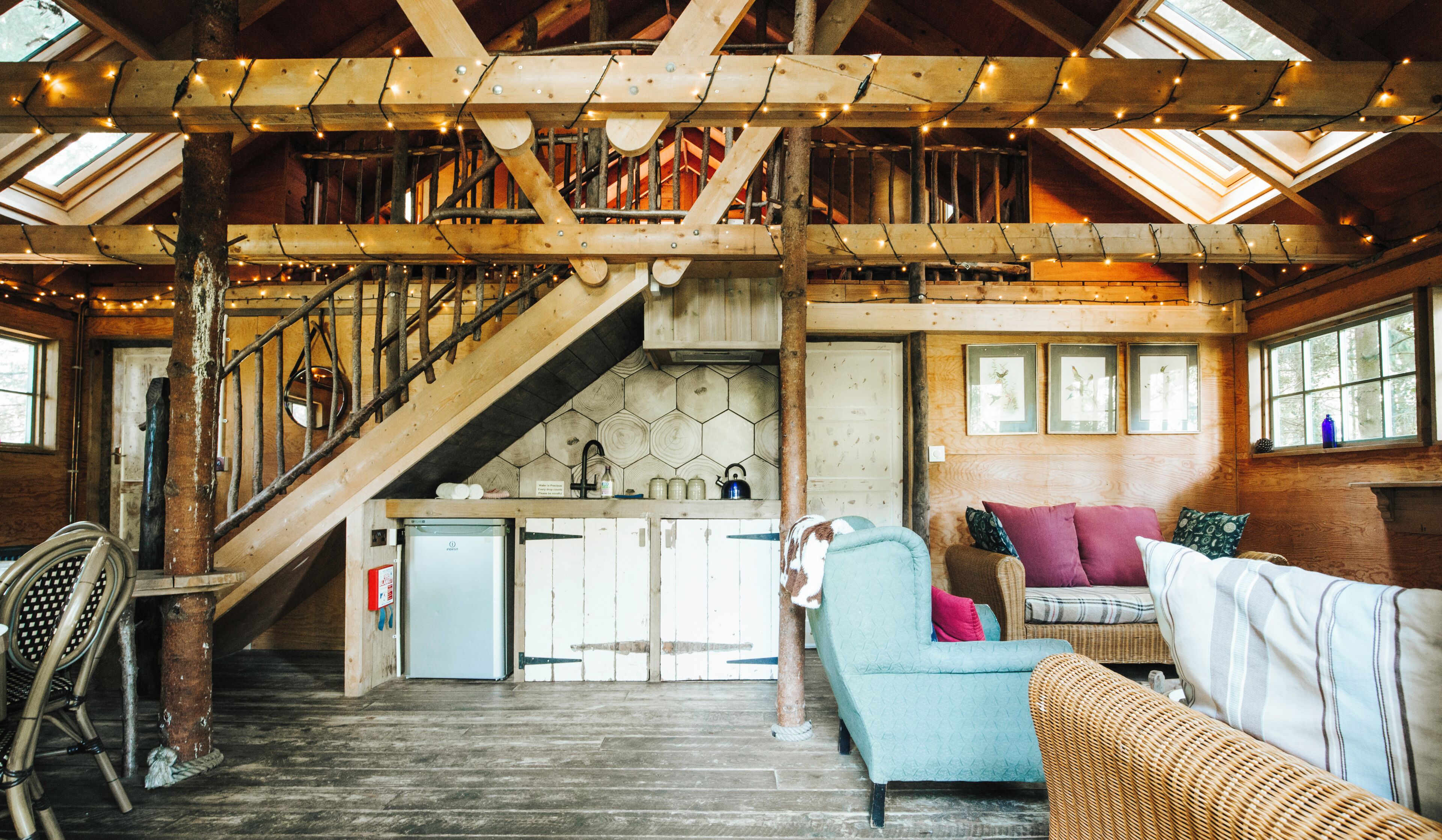 Un interior rústico con una escalera de madera, una kitchenette y un área de estar con sofá y sillones.