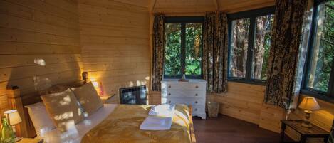 Un dormitorio de cabaña de madera con una cama, mesitas de noche, un aparador y una ventana con cortinas.