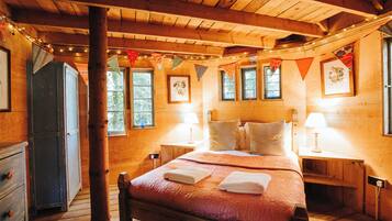 Un dormitorio de cabaña de madera con una cama, dos mesitas de noche, un armario y una ventana con cortinas.