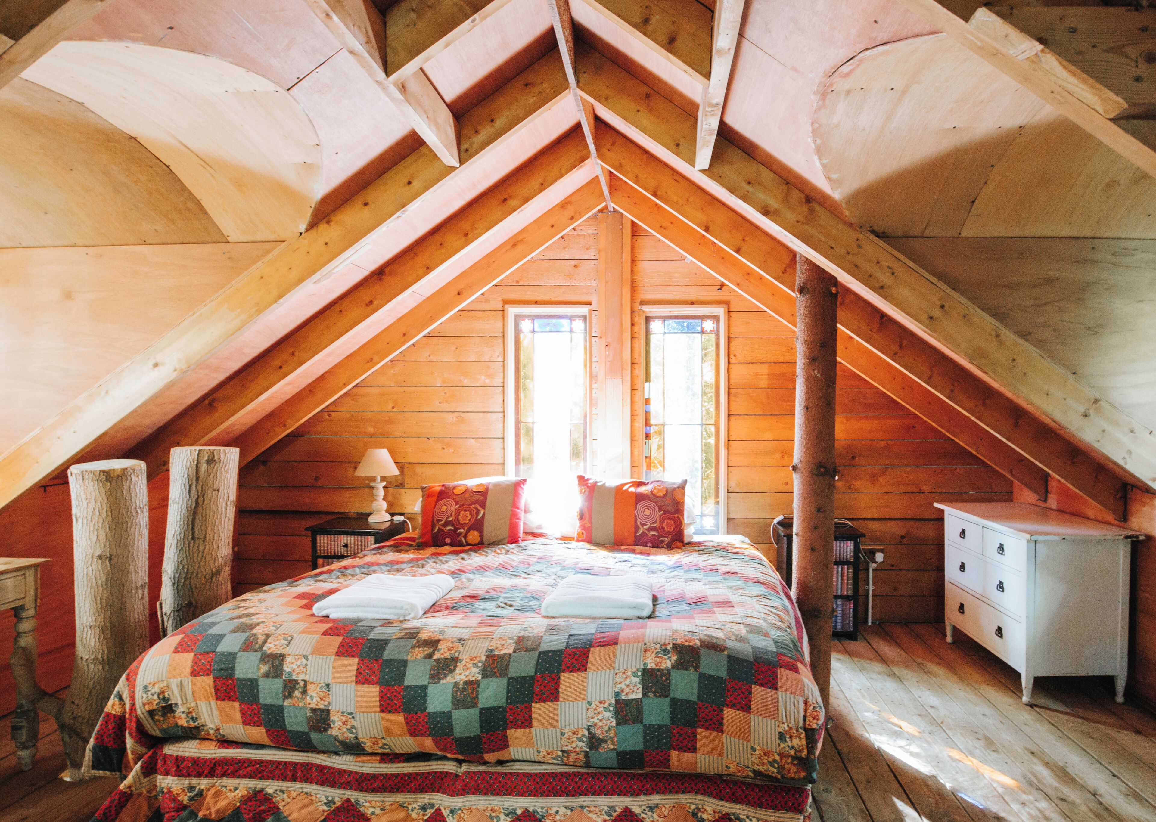 A bedroom with a sloped ceiling, a bed with a quilt, a dresser, and a nightstand with a lamp.