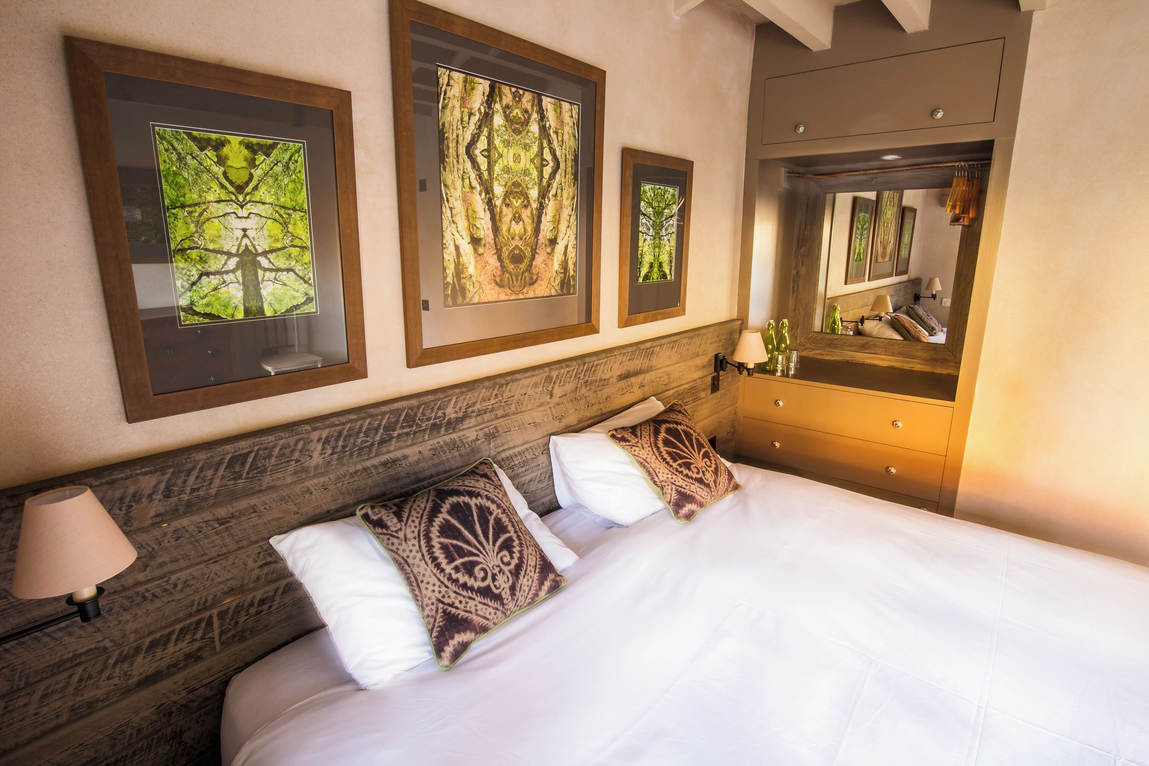 A hotel room with a bed, a dresser, a mirror, and framed artwork on the wall.