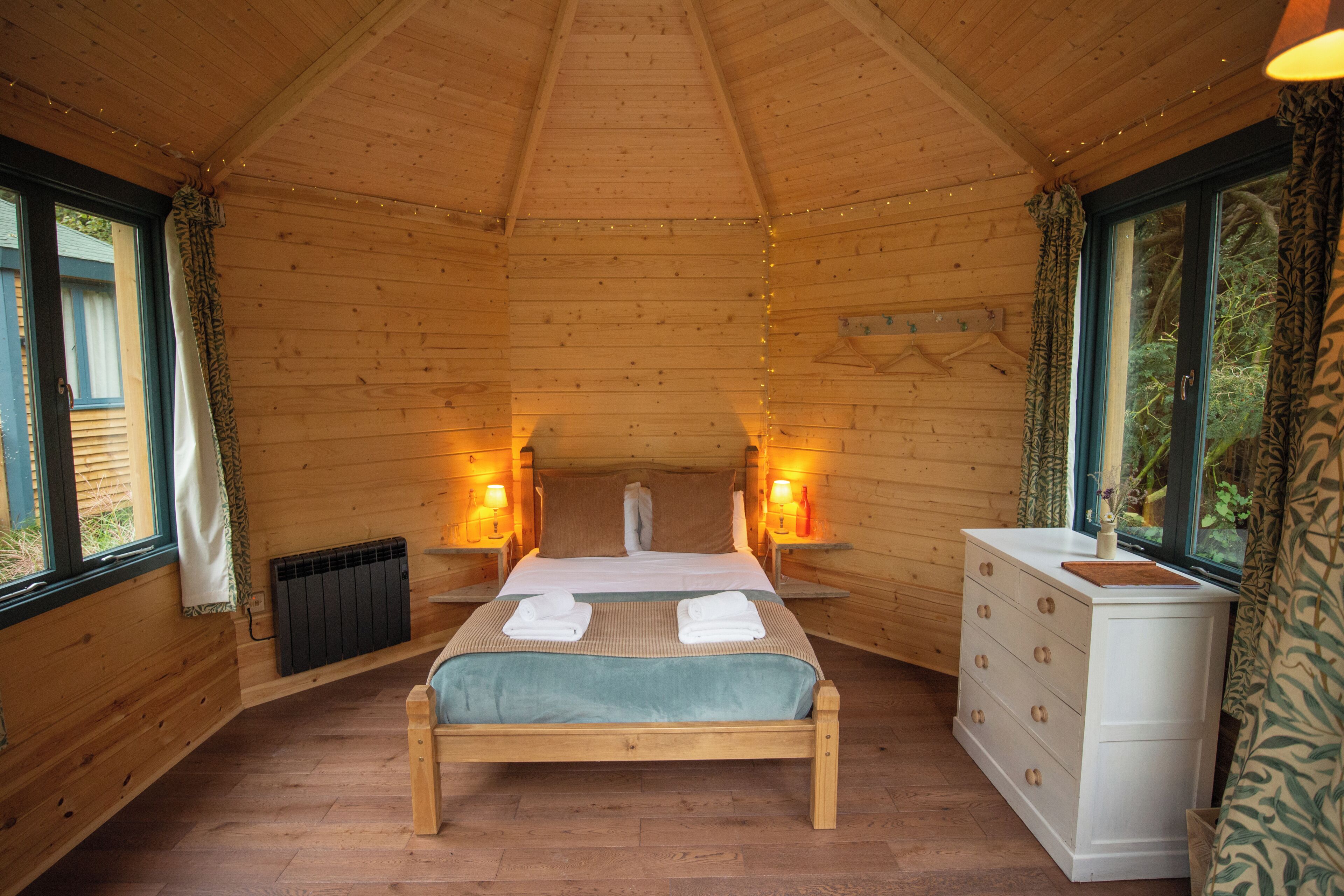 A wooden cabin bedroom with a bed, dresser, and two bedside lamps.