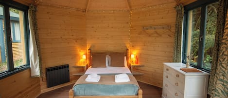 A wooden cabin bedroom with a bed, dresser, and two bedside lamps.