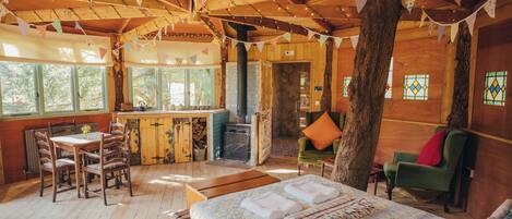 A rustic wooden cabin with a dining area, a kitchen, and a cozy living space with a bed.