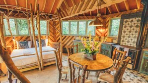 A rustic cabin interior with a wooden dining table, chairs, a bed, and a kitchen area. - West Lexham Wellness and Retreat Centre (King's Lynn)