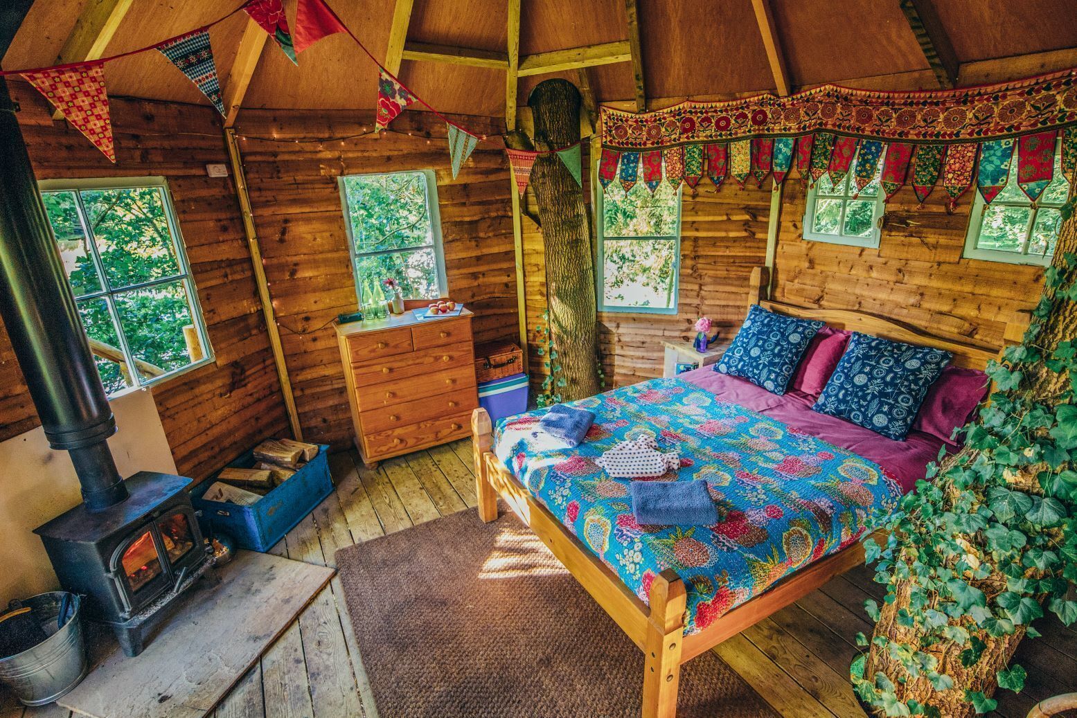 Interior acogedor de una cabaña con una cama de madera, chimenea, cómoda y ventana con vista a árboles.