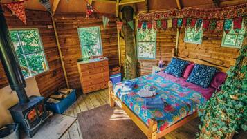 Interior acogedor de una cabaña con una cama de madera, chimenea, cómoda y ventana con vista a árboles.