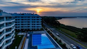 A modern hotel with a rooftop pool, a view of the sunset over a body of water, and a road adjacent to the property. - Apartment in Rogowo Near Beach and Lake (Trzebiatow)