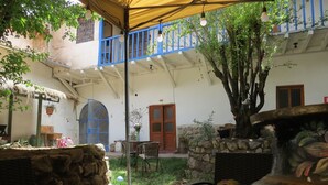 Uma área de pátio ao ar livre com um telhado de palha, paredes de pedra e uma árvore.