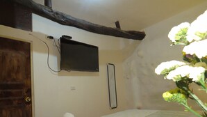 Um quarto com uma cama, televisão fixada na parede, porta de madeira e toalha branca sobre a cama.