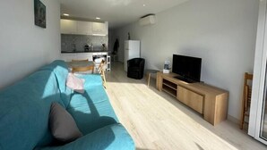 Una sala de estar moderna con un sofá, una televisión y una cocina al fondo.
