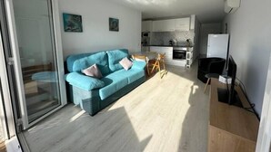 Un apartamento moderno con sala de estar, kitchenette y puerta corrediza de vidrio que da a un balcón.