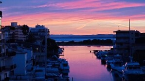 Un puerto deportivo con barcos amarrados, rodeado de edificios, y un cielo al atardecer.