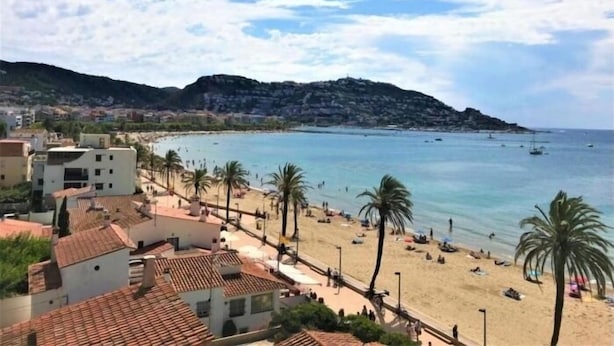 Un pueblo costero con una playa de arena, palmeras y una montaña al fondo.