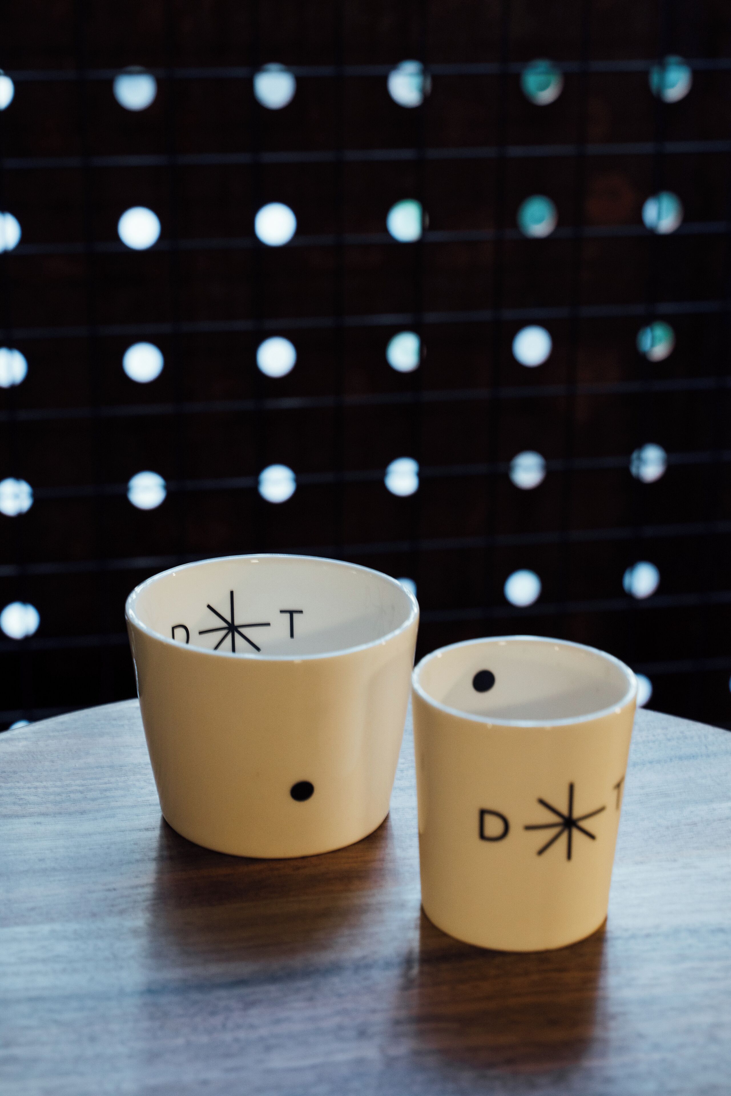 Two beige cups with symbols on a wooden table against a dark background with circular patterns.