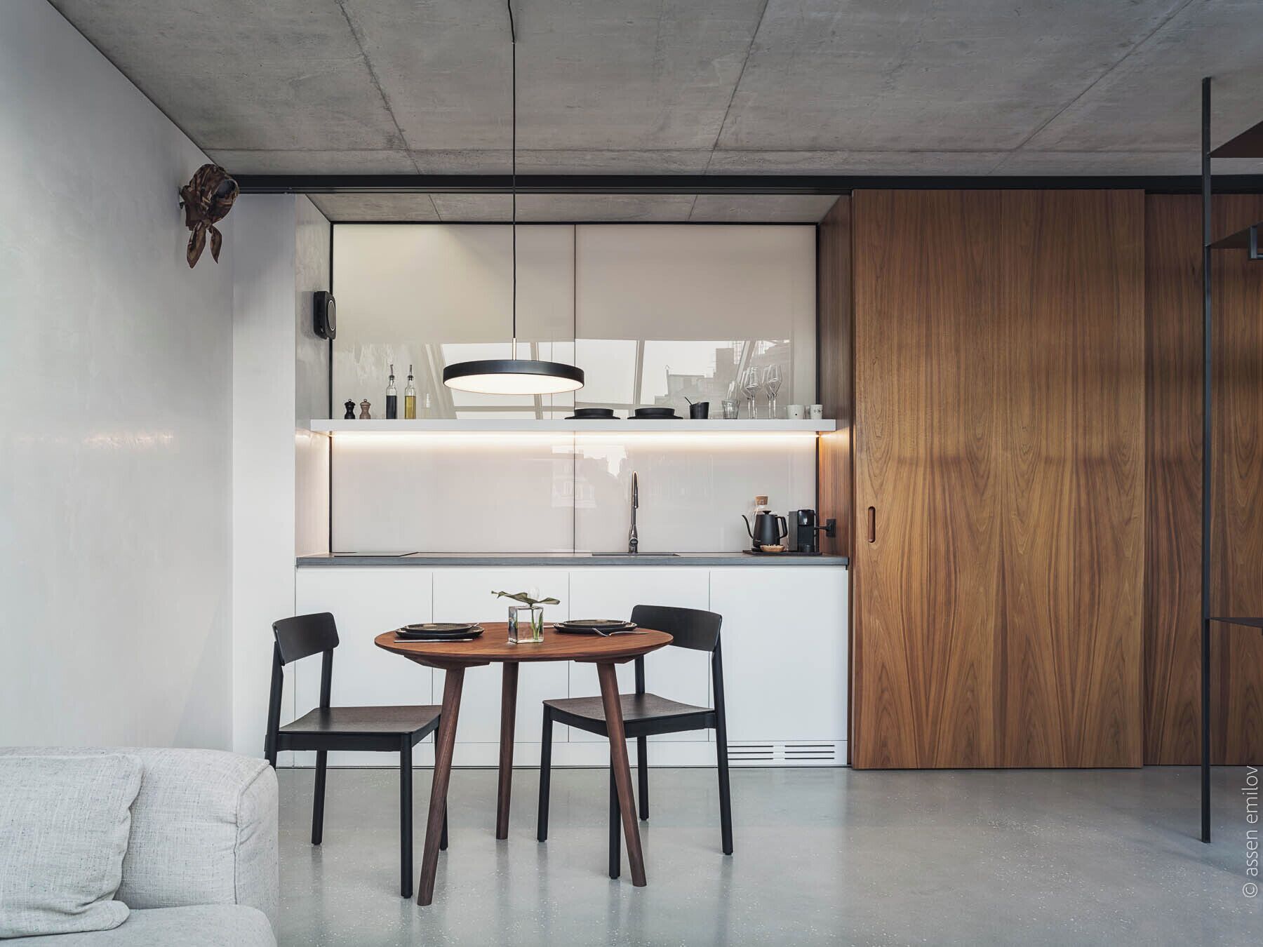 Une cuisine moderne avec un coin repas, comprenant une table ronde, deux chaises, un luminaire suspendu et un meuble en bois.