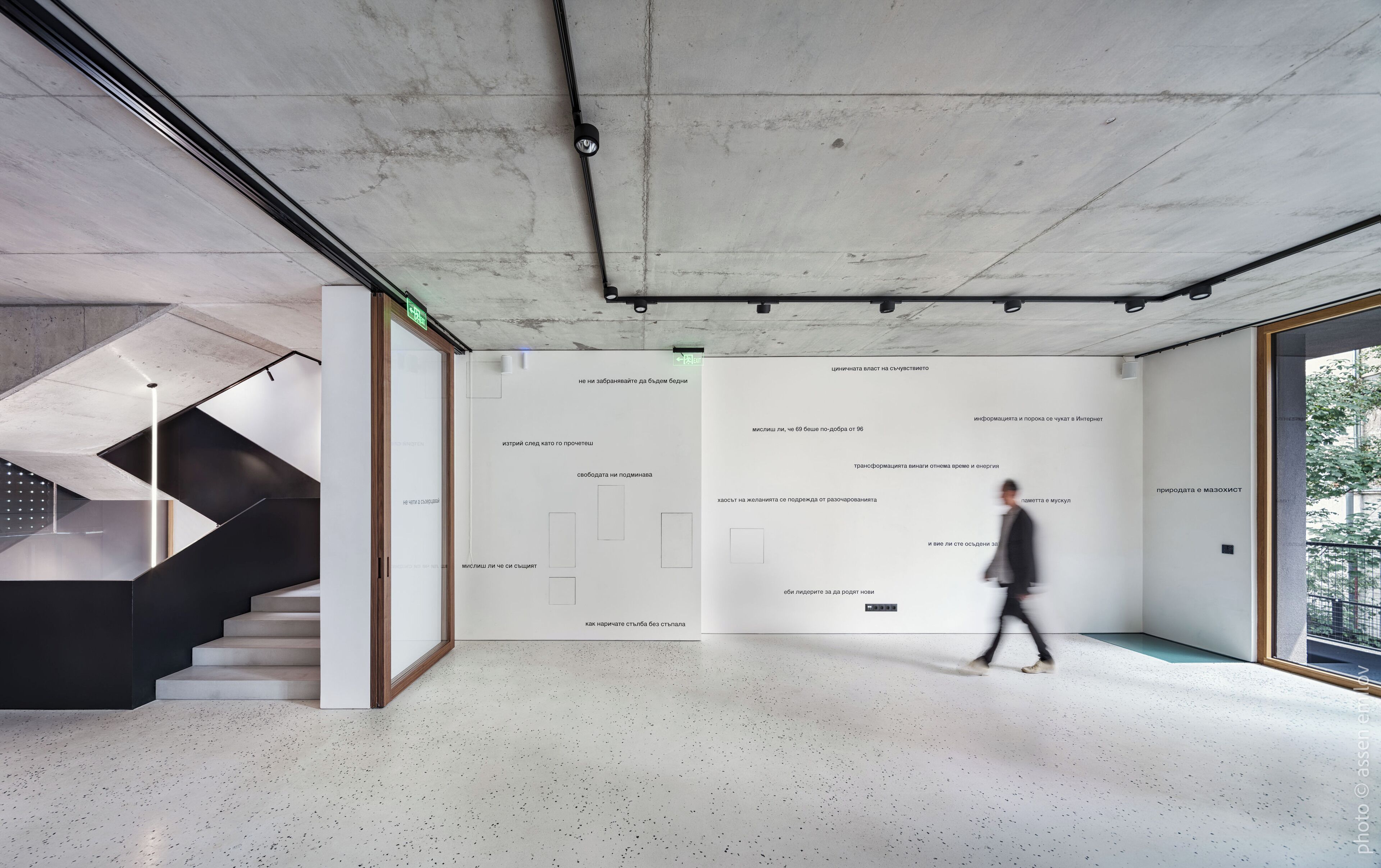 A modern interior with a staircase, a large wall with text, and a view through a glass door.