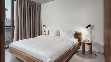 Un dormitorio moderno con una cama de madera, dos mesitas de noche con lámparas, vistas a través de un ventanal grande y un techo de hormigón.