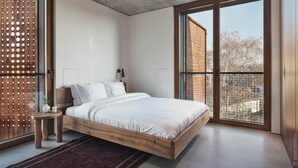 A modern bedroom with a large bed, a small bedside table, a nightstand, and a view of the city through large windows. - DOT Sofia (Sofia)