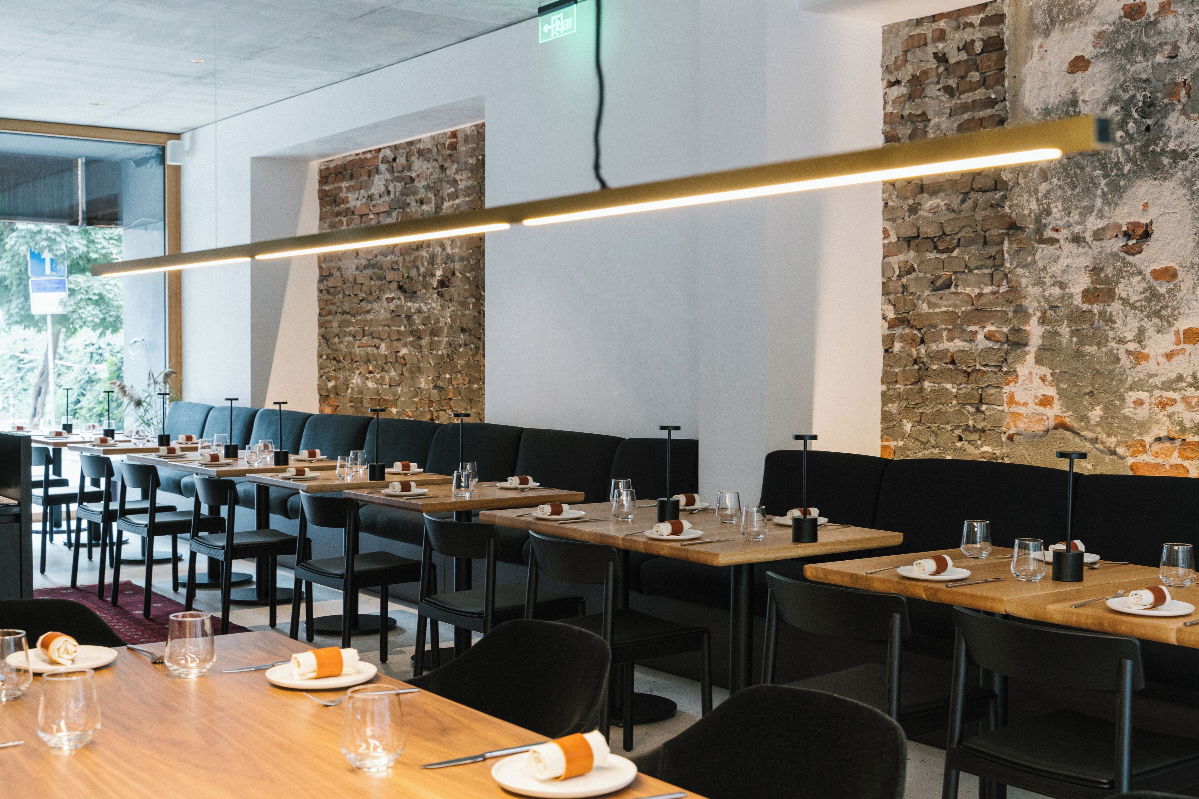 A restaurant with long communal tables, black chairs, and a brick wall.