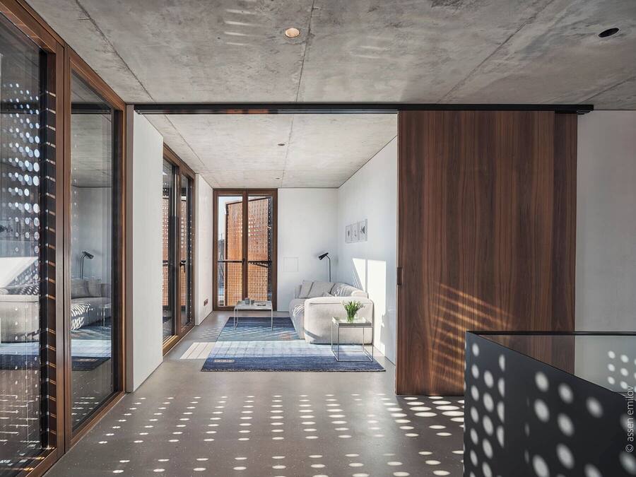 A modern interior with a concrete ceiling, a glass door leading to a balcony, a blue rug, and a white sofa.