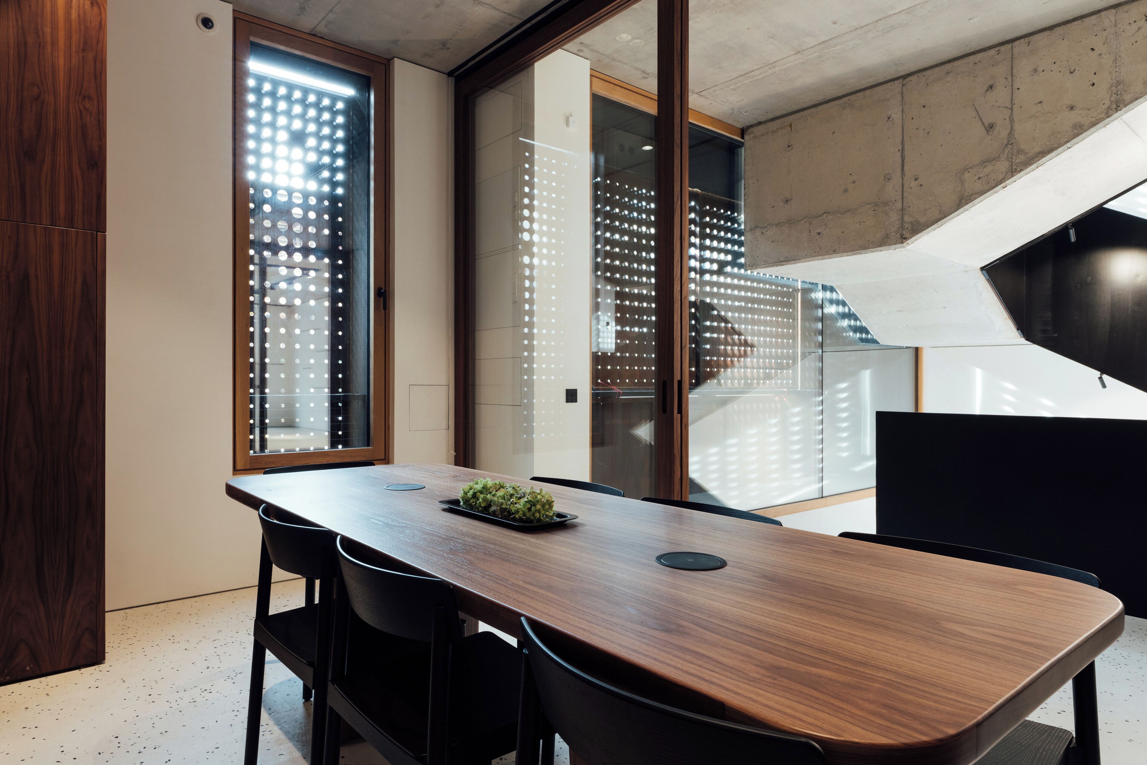 Een moderne vergaderruimte met een lange houten tafel, zwarte stoelen en een glazen scheidingswand.
