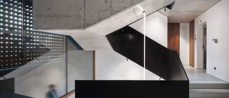 A modern staircase with a glass railing, a black platform, and a concrete ceiling.