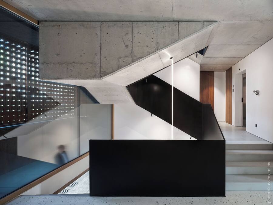 A modern staircase with a glass railing, a black platform, and a concrete ceiling.
