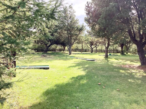 A grassy outdoor area with trees and a wooden bench. - Cabin in Camping Resort-shared Bathroom (Pandrup)