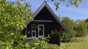 Une petite cabane aux couleurs sombres, dotée d’un toit à deux versants et entourée de verdure.
