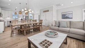 Una cocina moderna con armarios blancos, una mesa de comedor de madera e iluminación colgante.