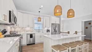 Una cocina moderna con armarios blancos, electrodomésticos de acero inoxidable y una isla central con taburetes de bar.