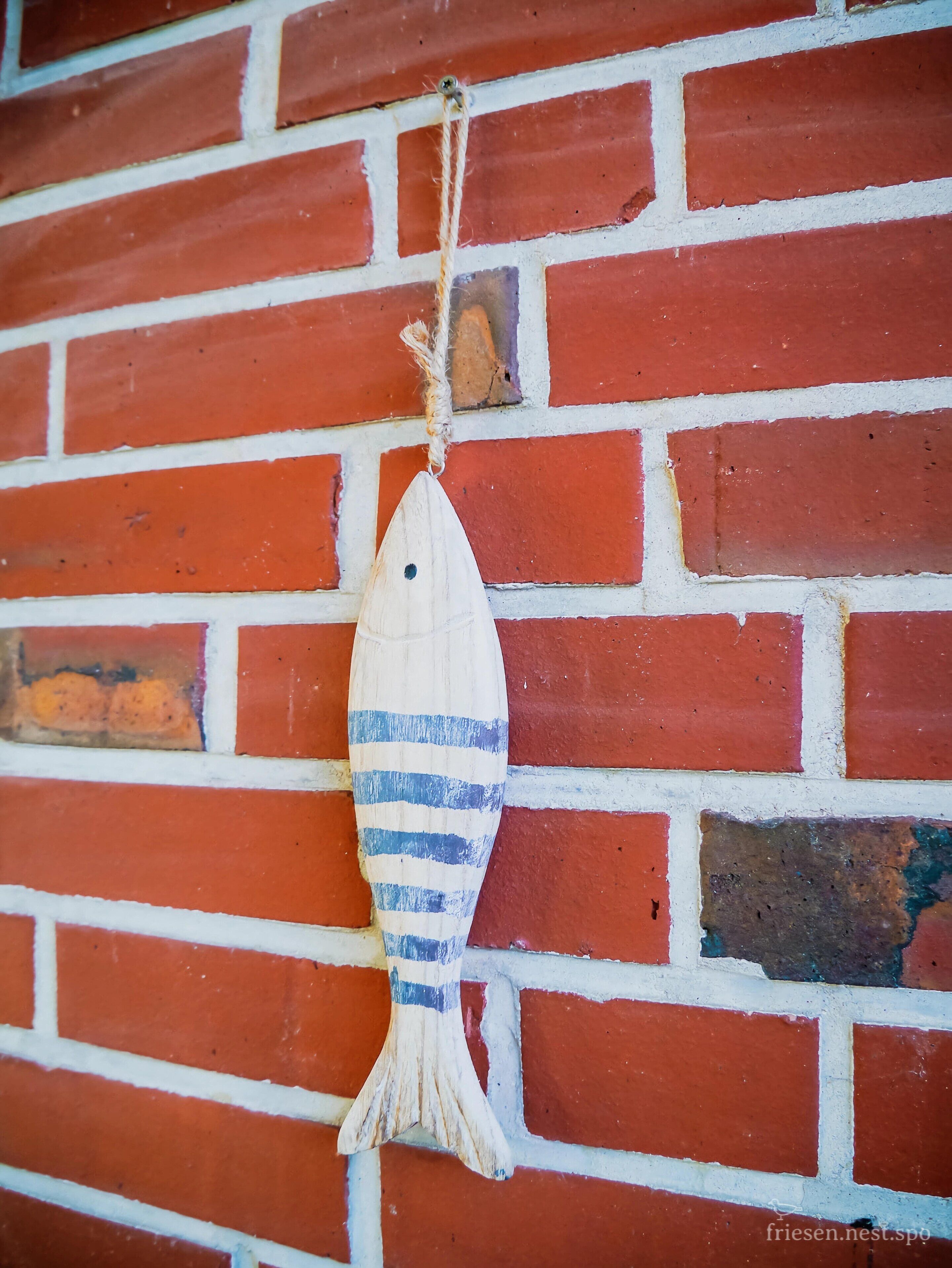 Eine Holz-Fischdekoration hängt an einer roten Backsteinwand.