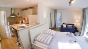 A modern hotel room with a bed, a small kitchenette, a sofa, and a window with curtains. - Ferienwohnung in St. Peter-ording (St. Peter-Ording)