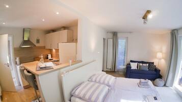 Una habitación de hotel moderna con una cama, una pequeña kitchenette, un sofá y una ventana con cortinas.