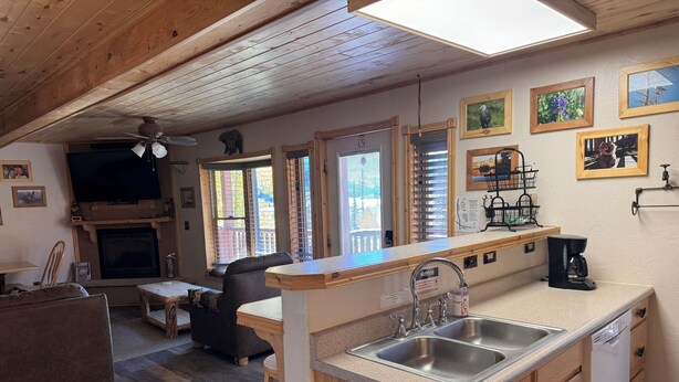 A cozy cabin-style room with a fireplace, wooden furniture, a kitchen area with a sink and coffee maker, and several framed pictures on the walls. - OPEN YEAR ROUND - 3 Bedroom Lake San Cristobal Condo on the Alpine Loop (Lake City)